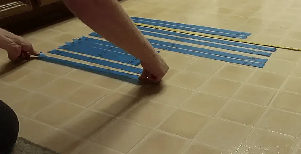 Hands measuring and applying blue painter's tape to the floor to plan a layout.