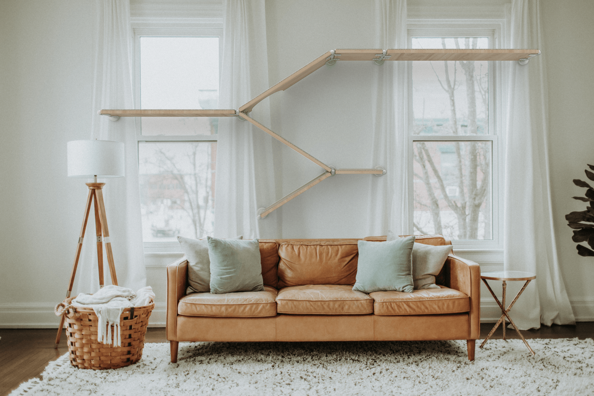 Modern living room with a wooden cat shelf system spanning across two windows above a tan leather sofa.