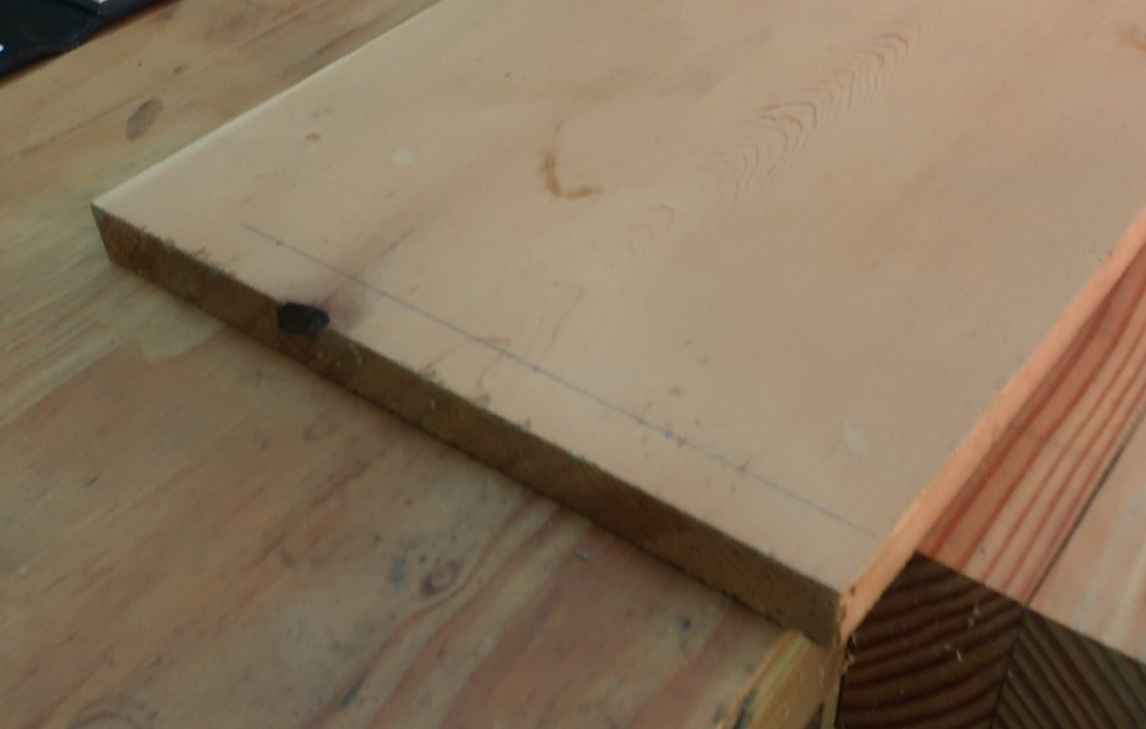 Light-colored wooden plank with a thin pencil line marked across the grain for cutting or clamping.
