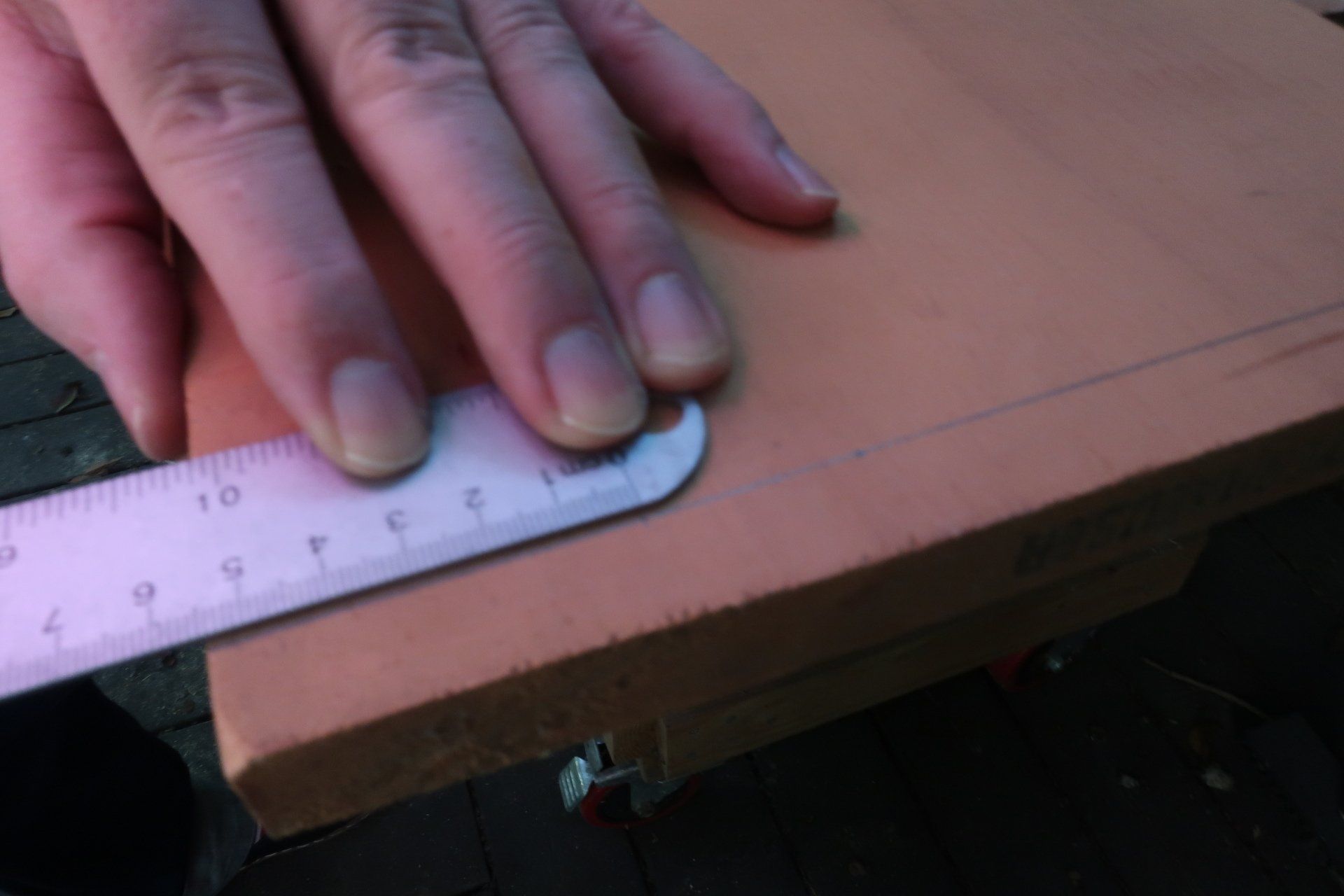 Close-up of a hand using a metal ruler to measure a precise line on a piece of light-colored wood.