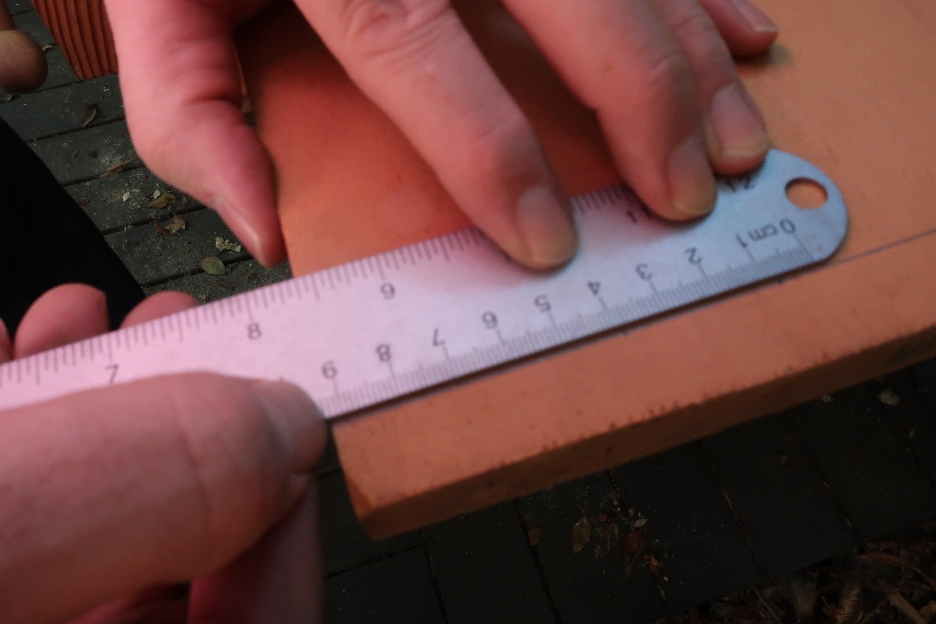 Close-up of a hand using a metal ruler to measure a precise line on a piece of light-colored wood.