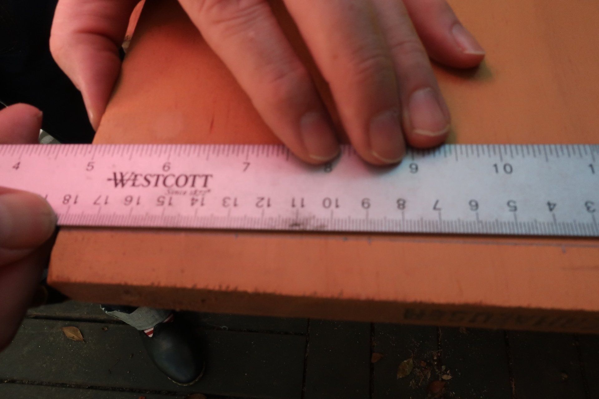 Close-up of a hand using a metal ruler to measure a precise line on a piece of light-colored wood.