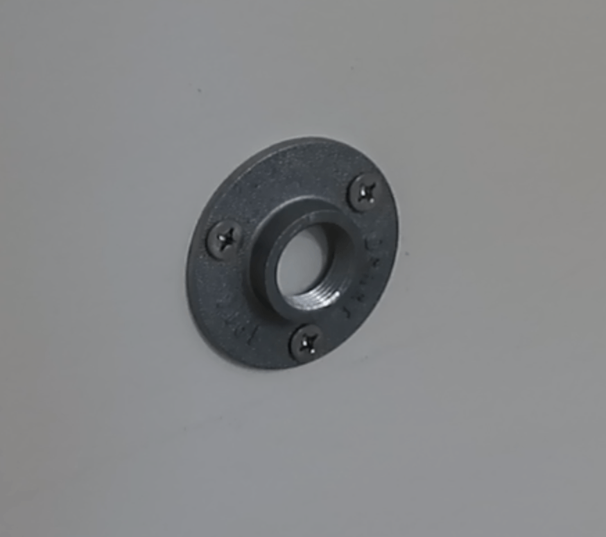 A dark grey metal floor flange secured to a wall with three screws.