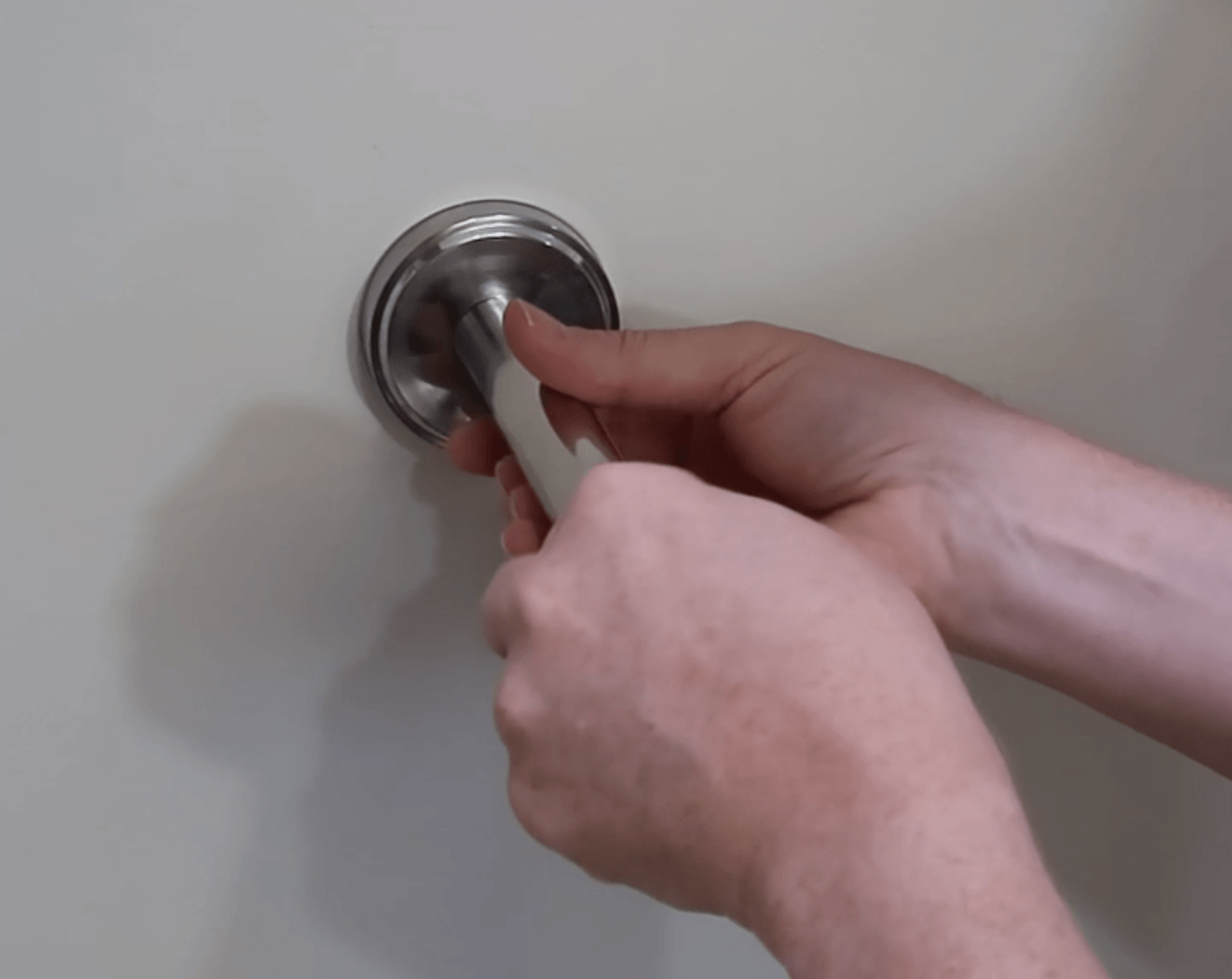 Hands screwing a support arm into a wall-mounted circular flange for a cat shelf installation.