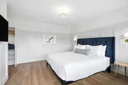 Bright bedroom with king bed, navy headboard, white bedding, wood floors, and closet.