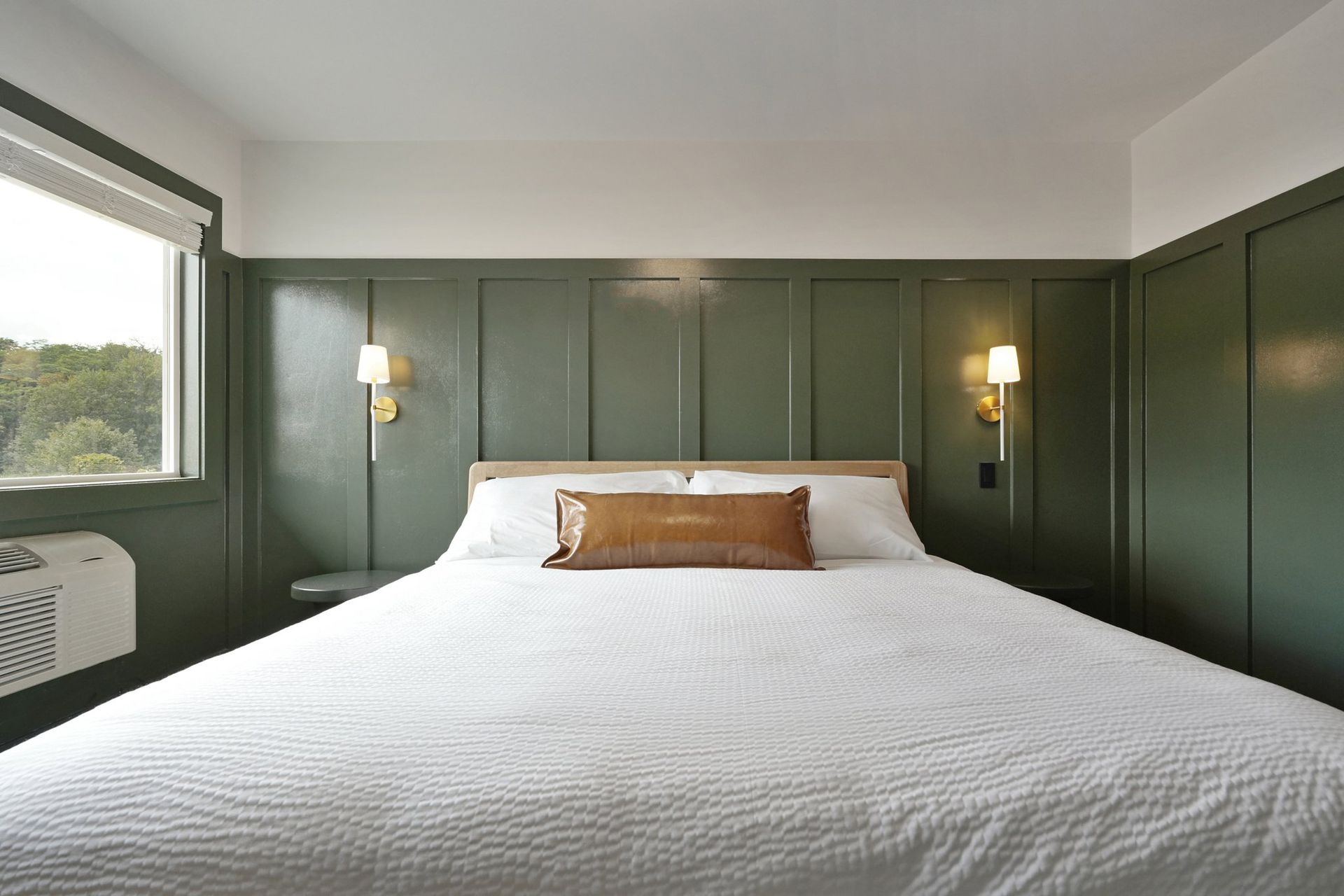Bedroom with a bed, green panelled wall, and two sconces.