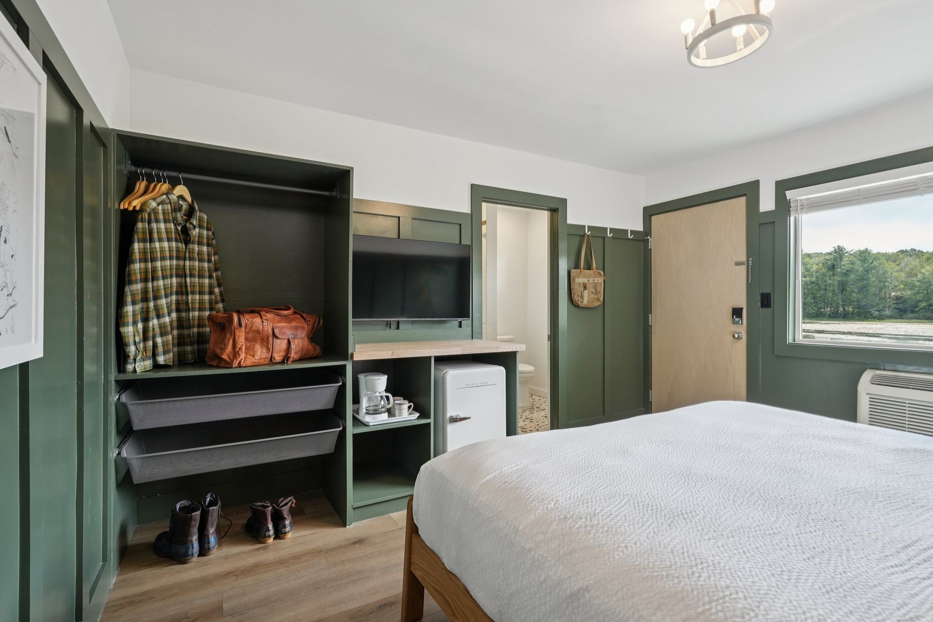 Green-walled hotel room with closet, bed, TV, mini fridge, and a window overlooking a lake.