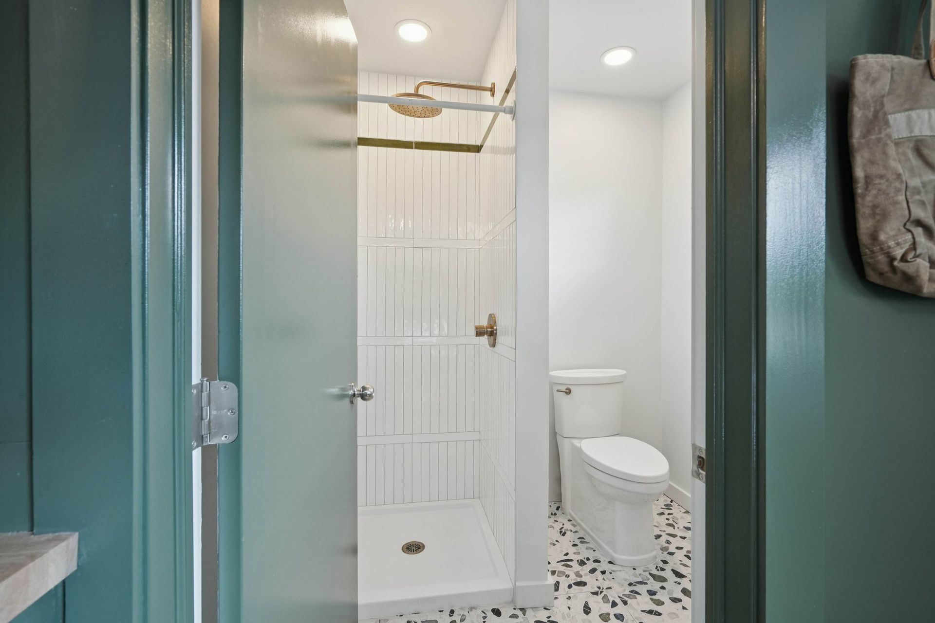 Bathroom with turquoise doorframe, white shower and toilet, pebble floor.