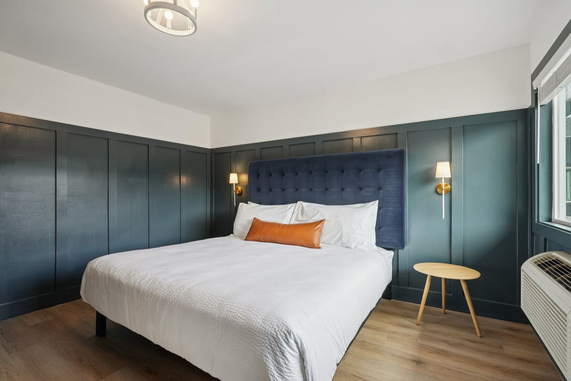 Bedroom with a bed, blue wall panels, a side table, and a window with air conditioning unit.