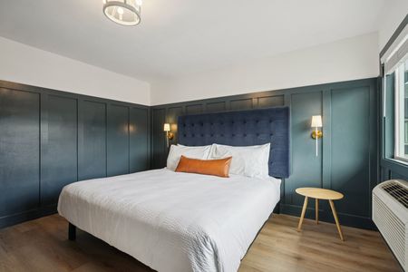 Bedroom with blue paneling, a bed, small table, and window.