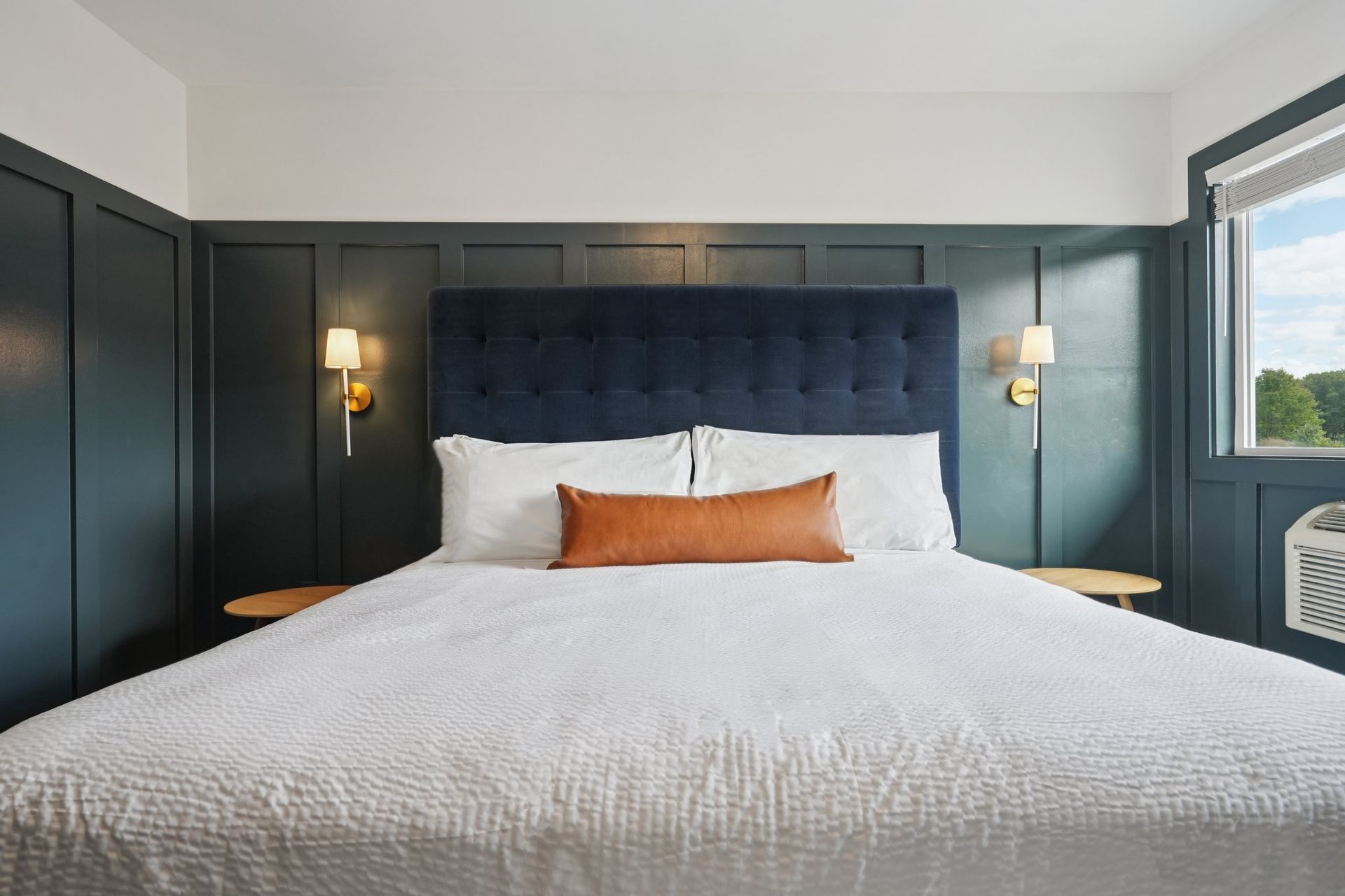 Bedroom with a bed, blue headboard, brown lumbar pillow, and dark blue paneling.