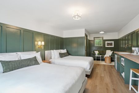 A hotel room with two beds, green paneling, and a small kitchen area.