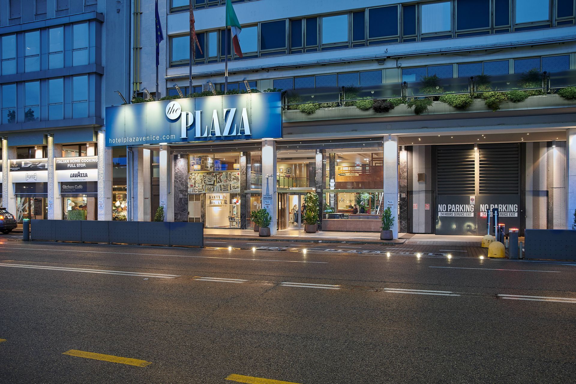 Entrance to Hotel Plaza, Milan, Italy. Blue sign over entrance. Street and building reflections.
