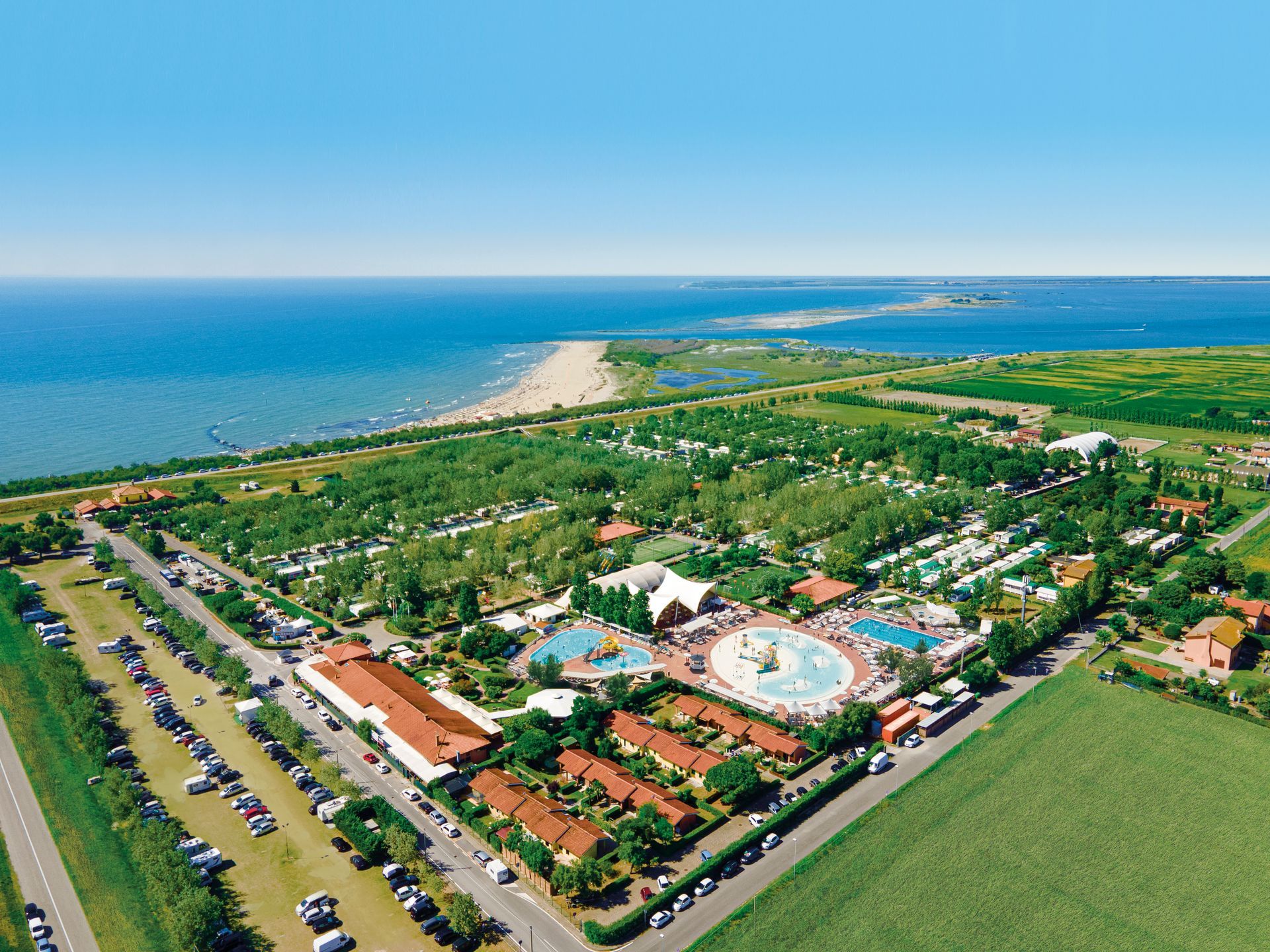 Vista aerea di un grande resort balneare con piscine, edifici, spazi verdi e una spiaggia.