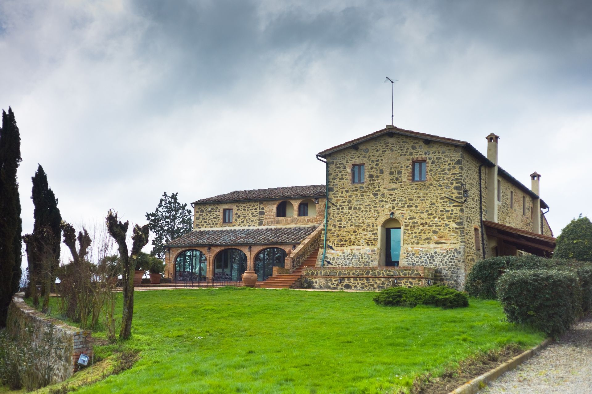 Edificio in pietra con finestre ad arco, prato verde e cielo nuvoloso.
