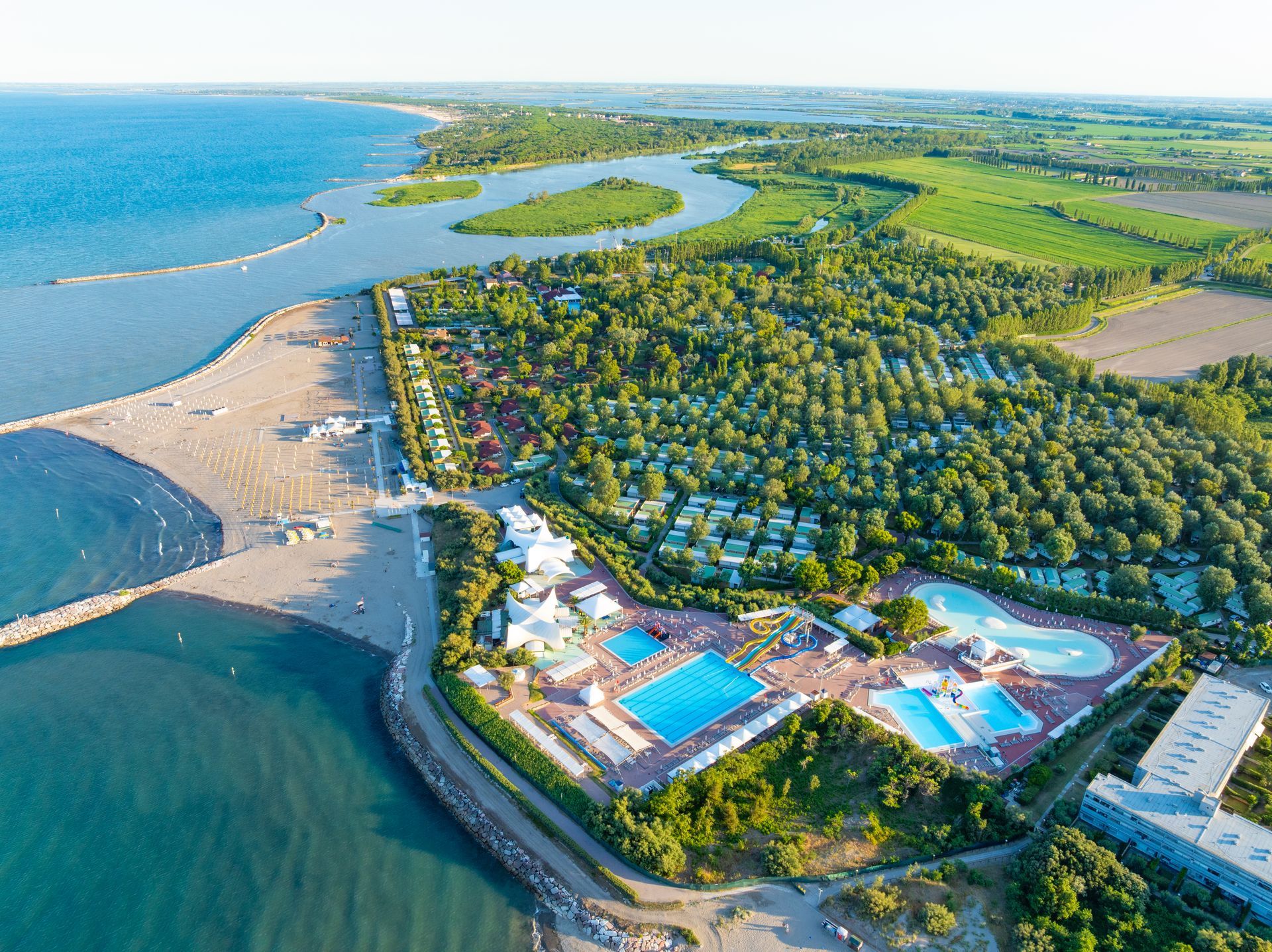 Vista aerea di un resort con spiaggia, piscine, alberi ed edifici vicino all'oceano.