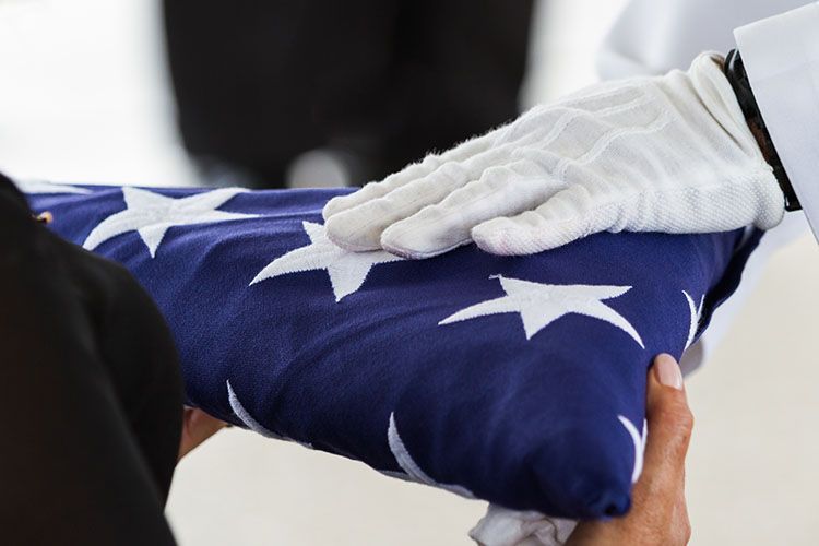 Gloved hands folding a blue American flag with white stars