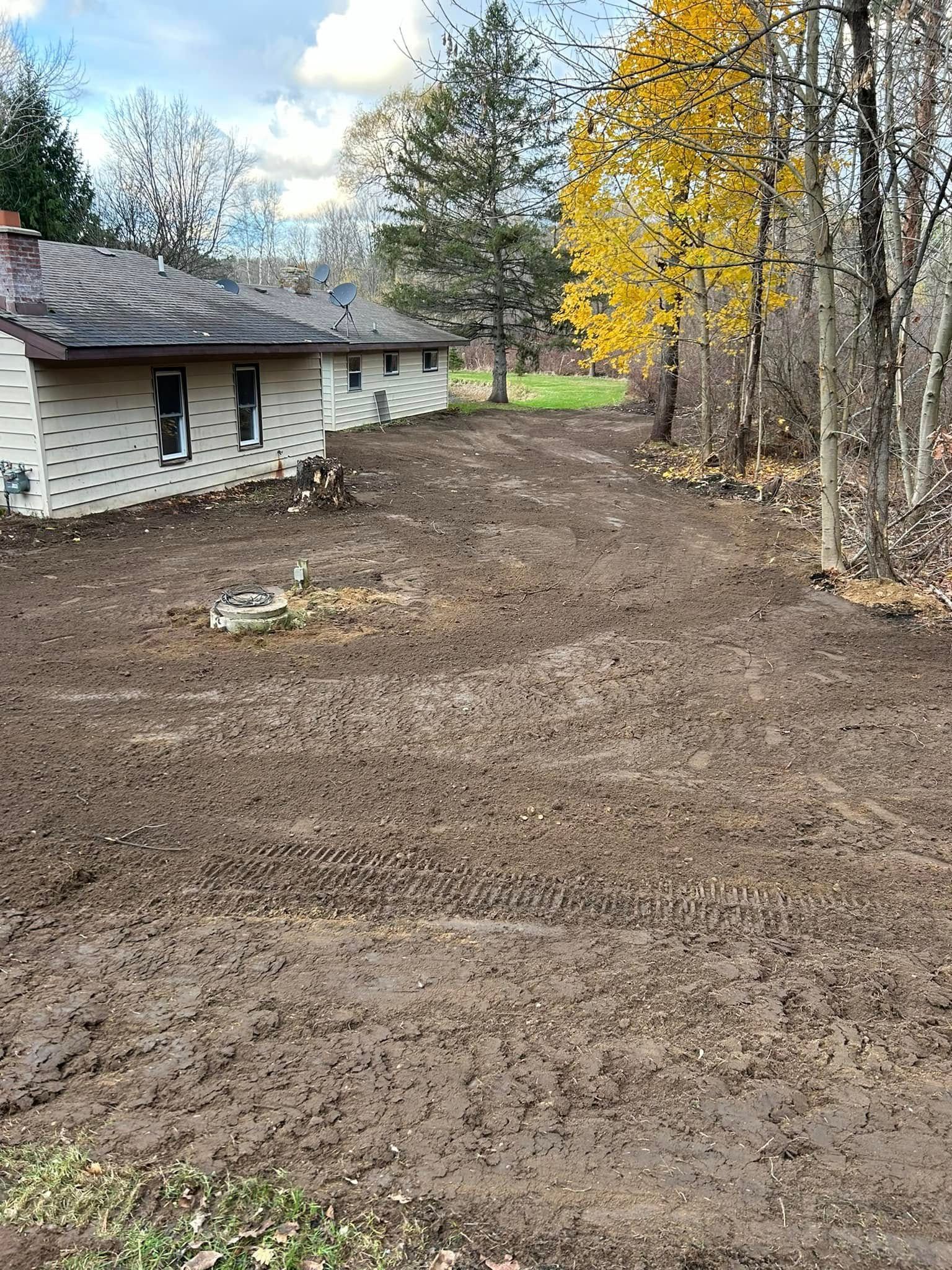 Rural yard beside a house, with freshly graded dirt and yellow autumn trees along the edge.
