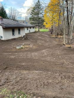 Rural yard beside a house, with freshly graded dirt and yellow autumn trees along the edge.