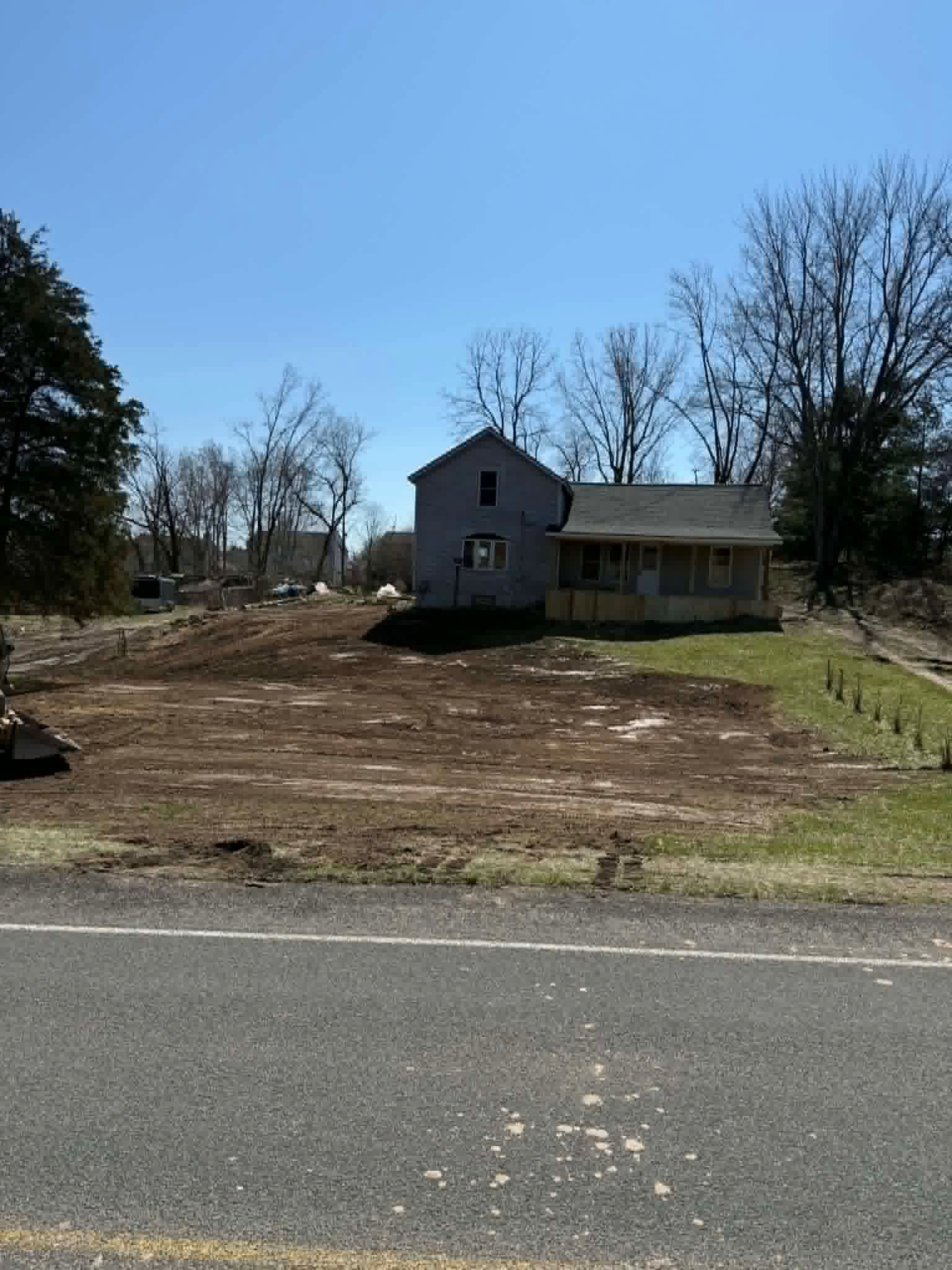 Small house on a cleared lot beside a road, with bare trees and a blue sky.