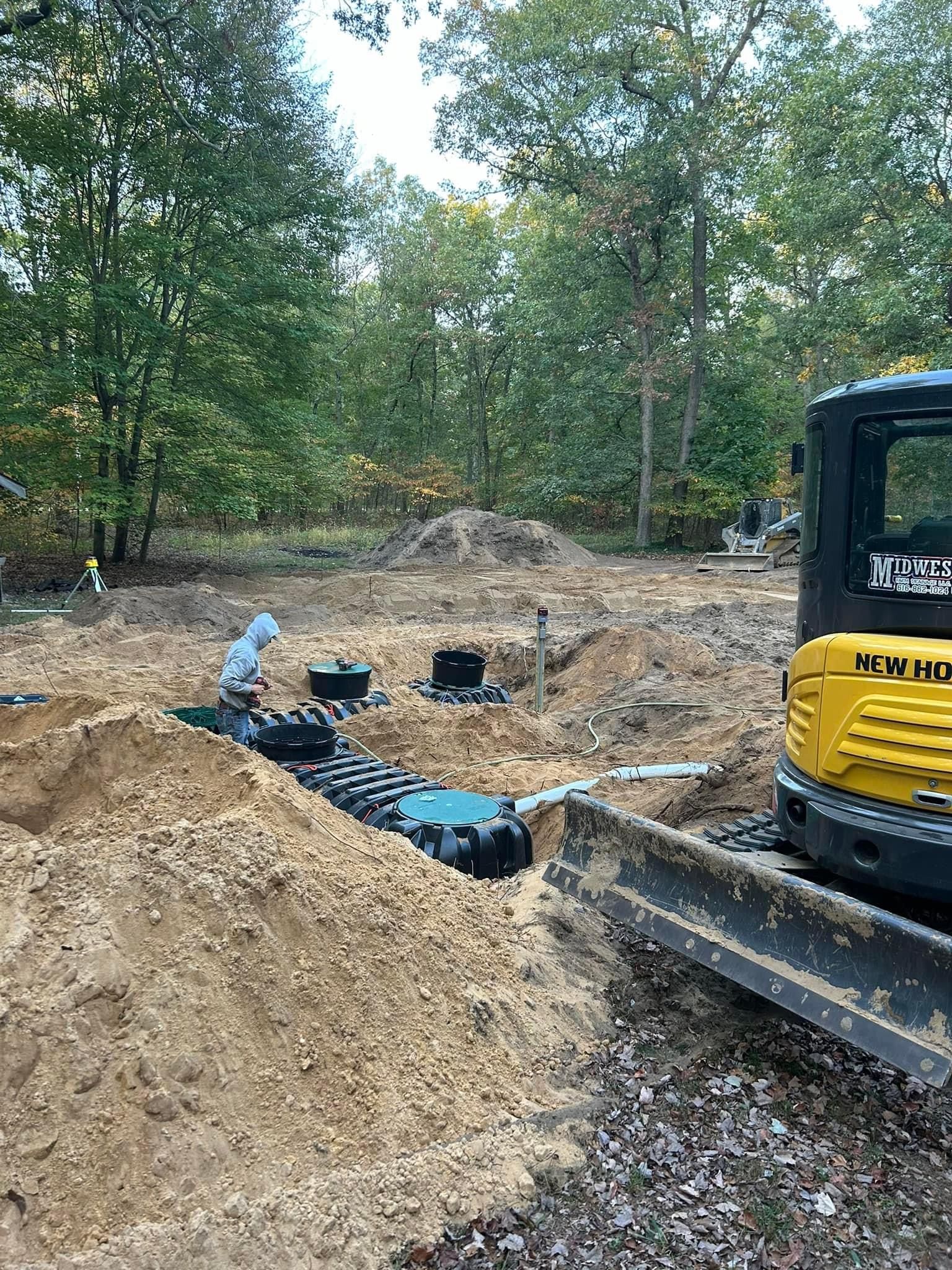 Excavator beside trenches and dirt piles at a wooded construction site