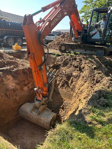 Excavator digging a deep trench in muddy ground at a construction site.