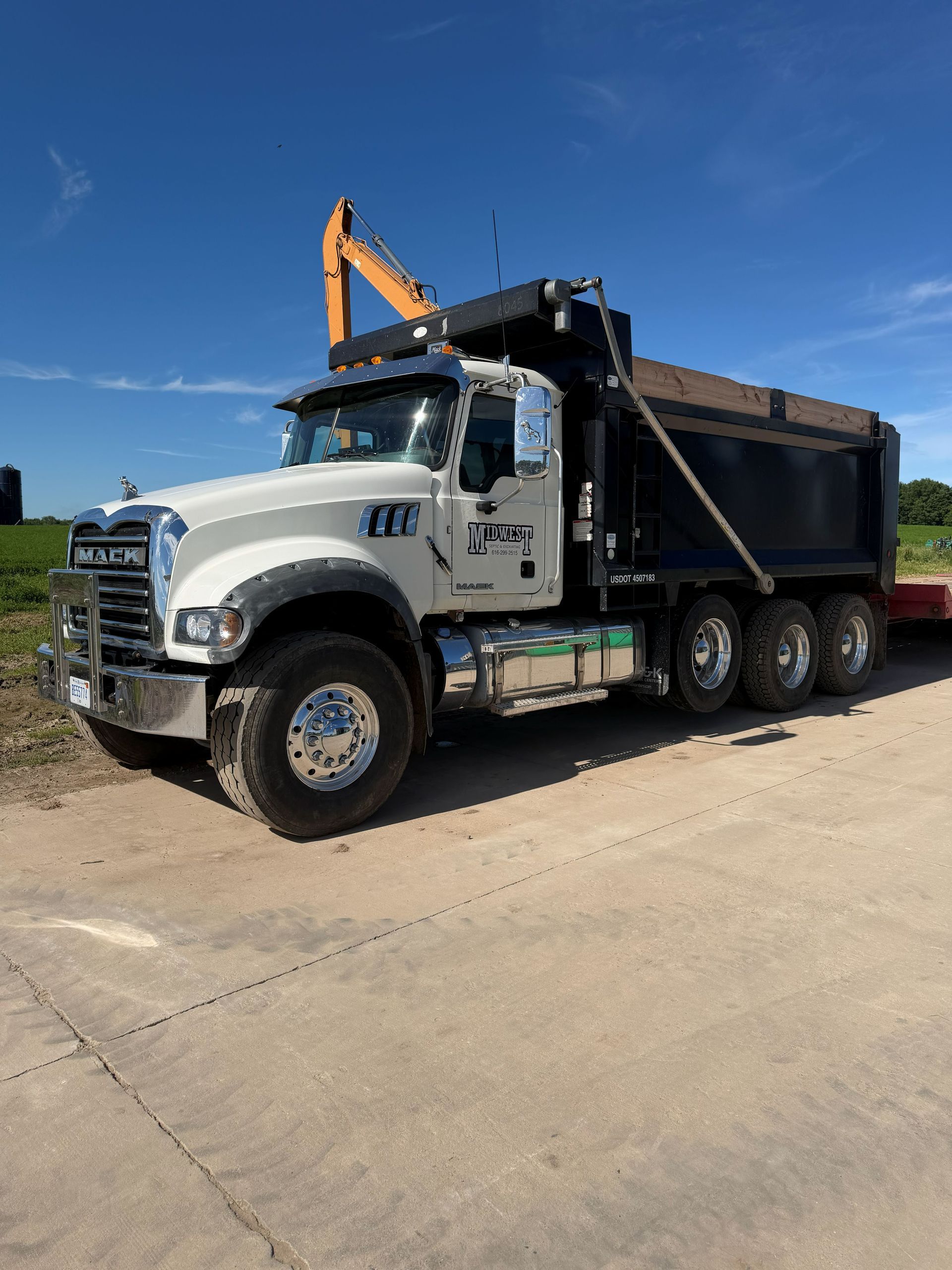 White dump truck with raised bed and orange crane parked on a sunny road under a clear blue sky