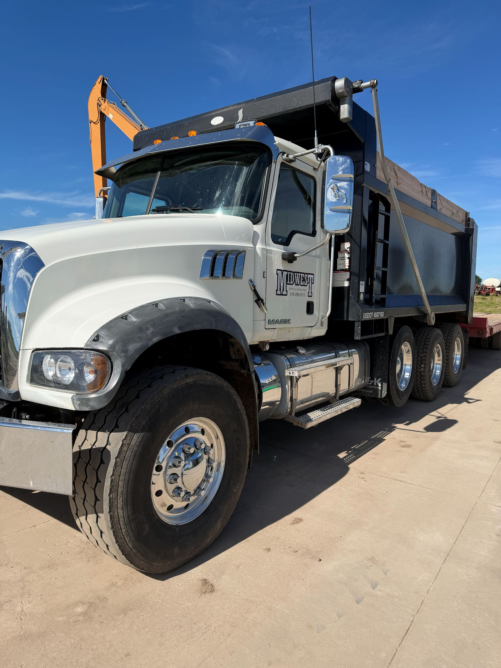 White dump truck parked on a sunny road, side view with raised black bed