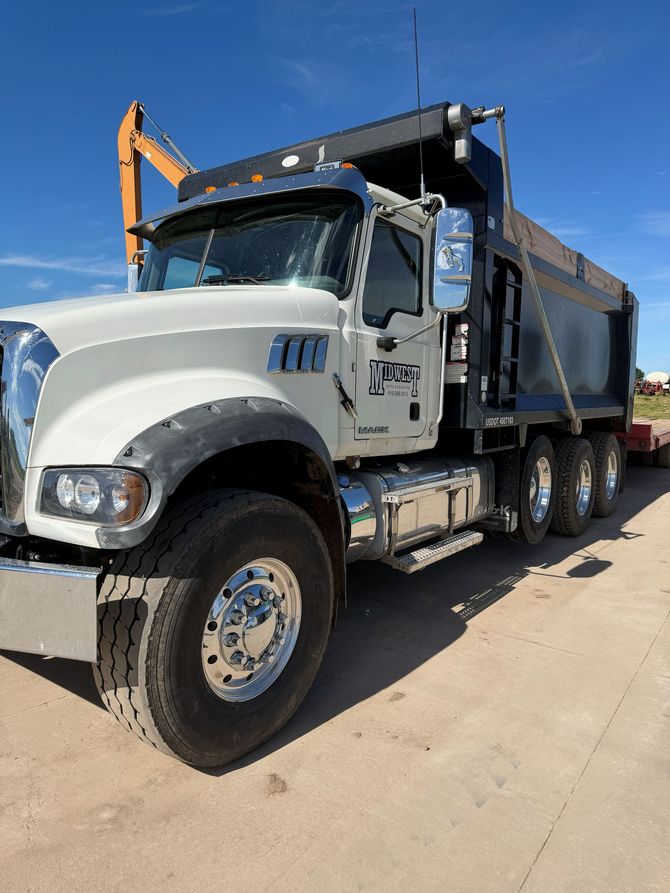 White dump truck parked on a sunny road, side view with raised black bed