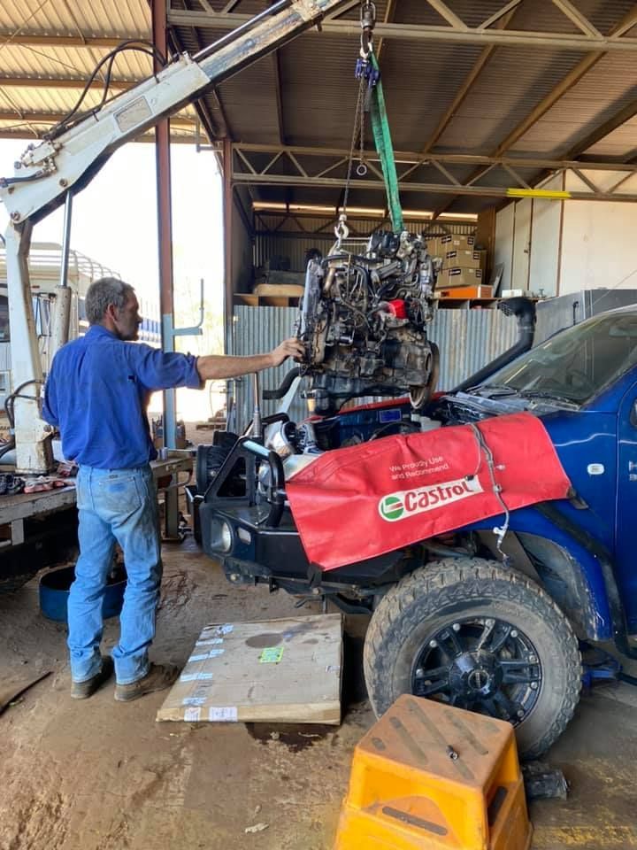 A Man Installing an Engine Into a Blue Truck in a Garage Using a Crane — Traction Diesel Services in Clermont, QLD