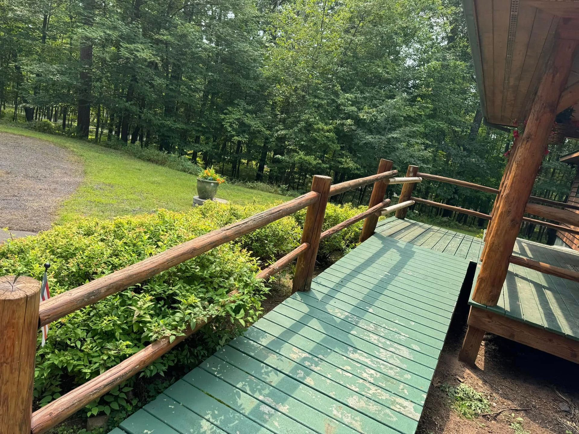 Wooden deck with green railing overlooking a leafy wooded path and garden