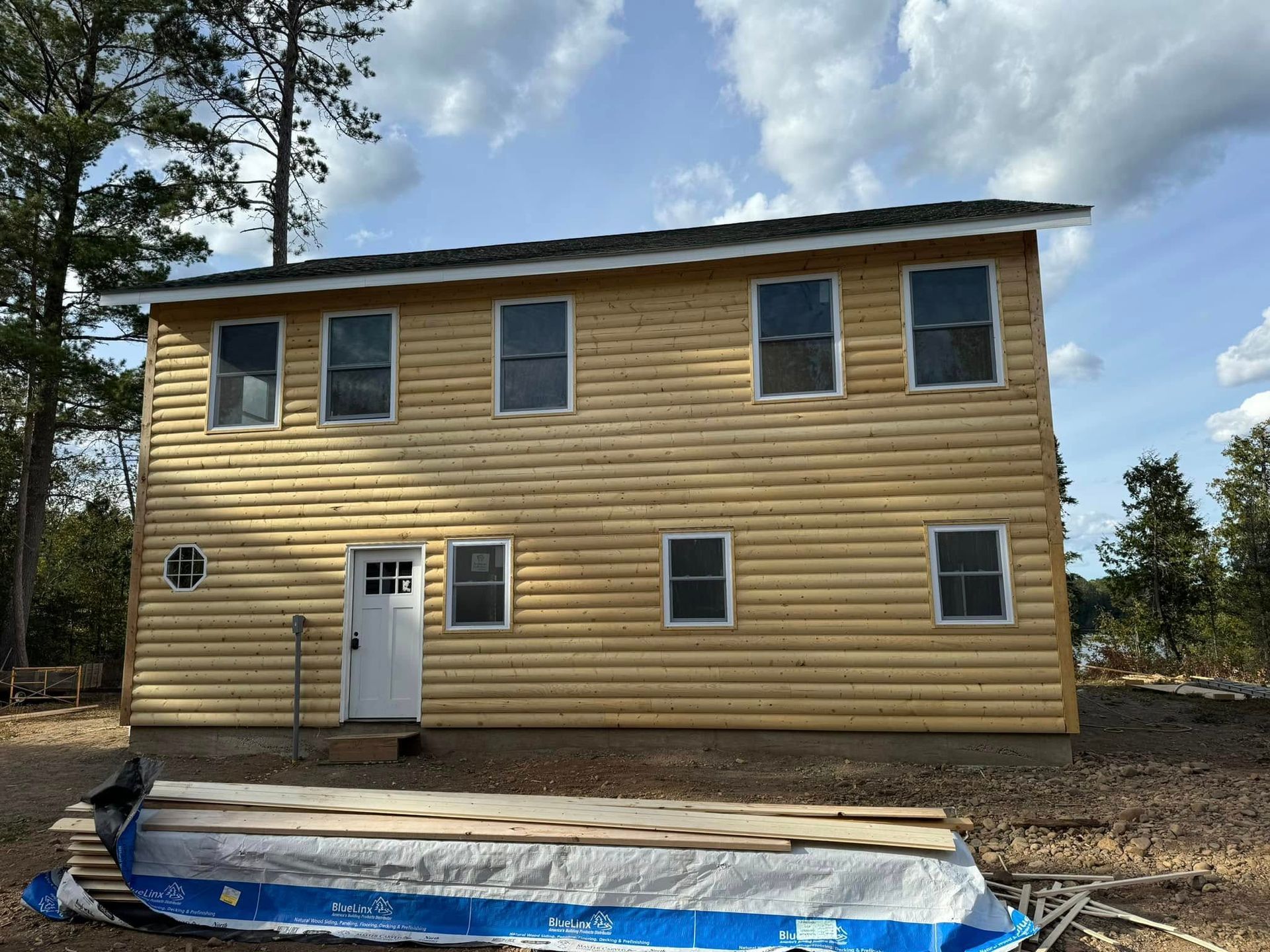Two-story tan house under construction with white trim and a blue tarp in front