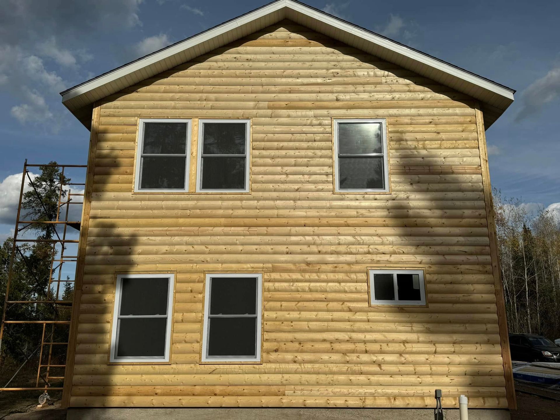 Rear view of a two-story wood-sided house with windows and a gable roof under a cloudy sky