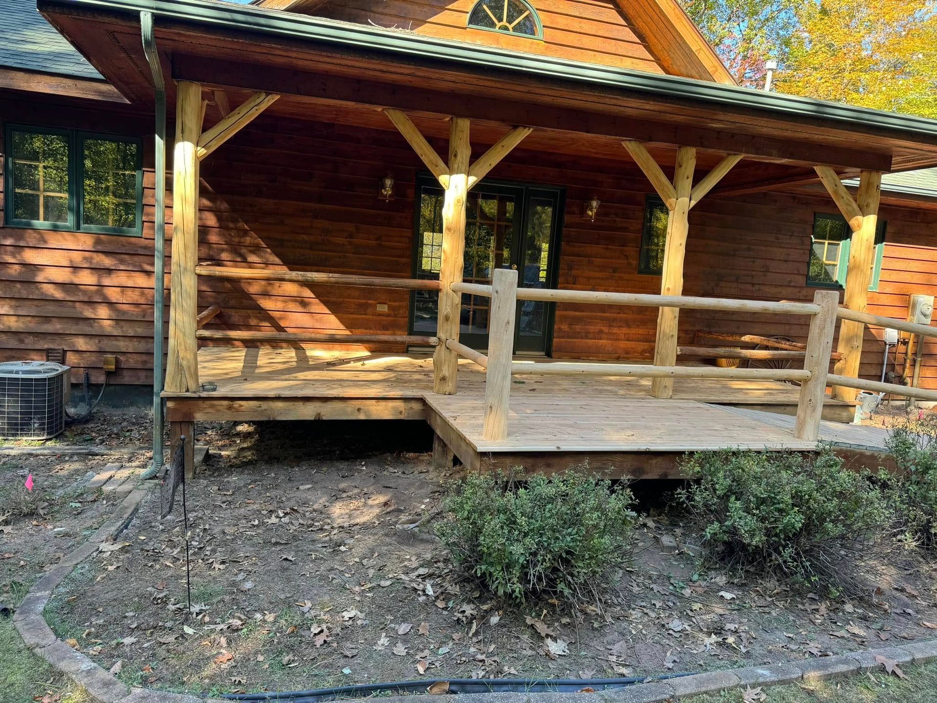Wooden cabin porch with railings, log walls, and stone steps in a wooded setting.