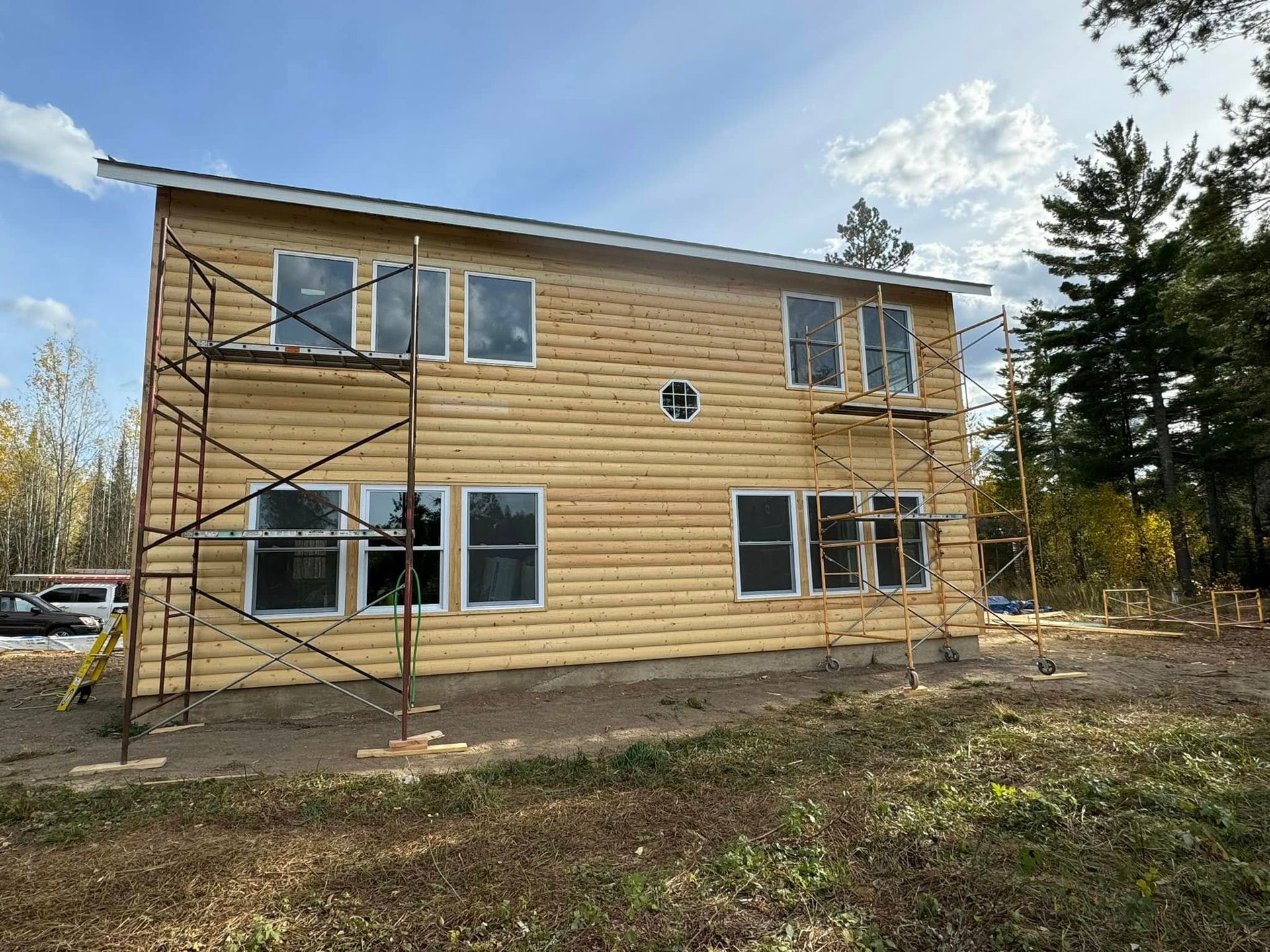 Two-story house under construction with exposed wood siding and scaffolding outside under a cloudy sky