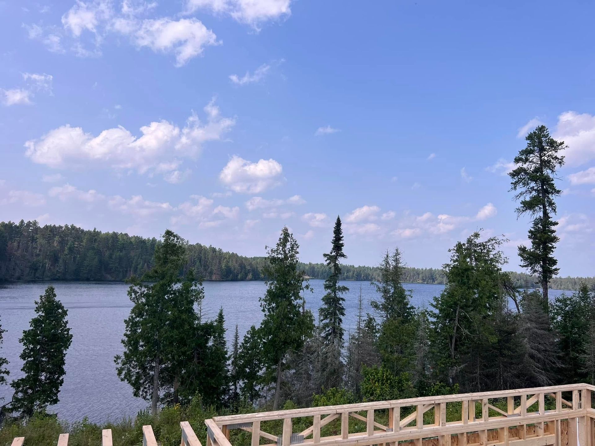 Lake view with blue sky, trees, and a wooden railing in the foreground