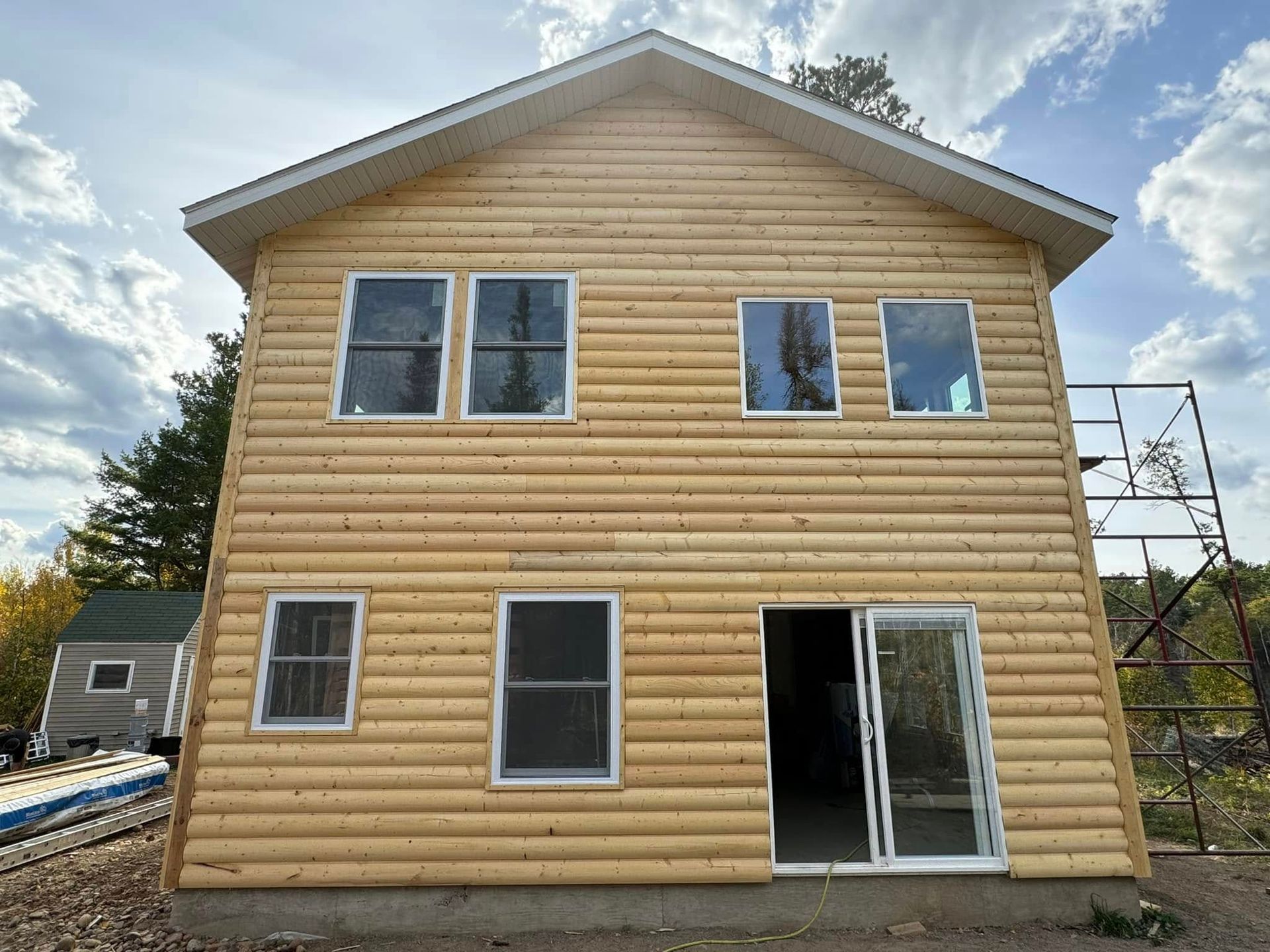 Two-story tan house with wood siding, white-trim windows, and a sliding glass door under construction