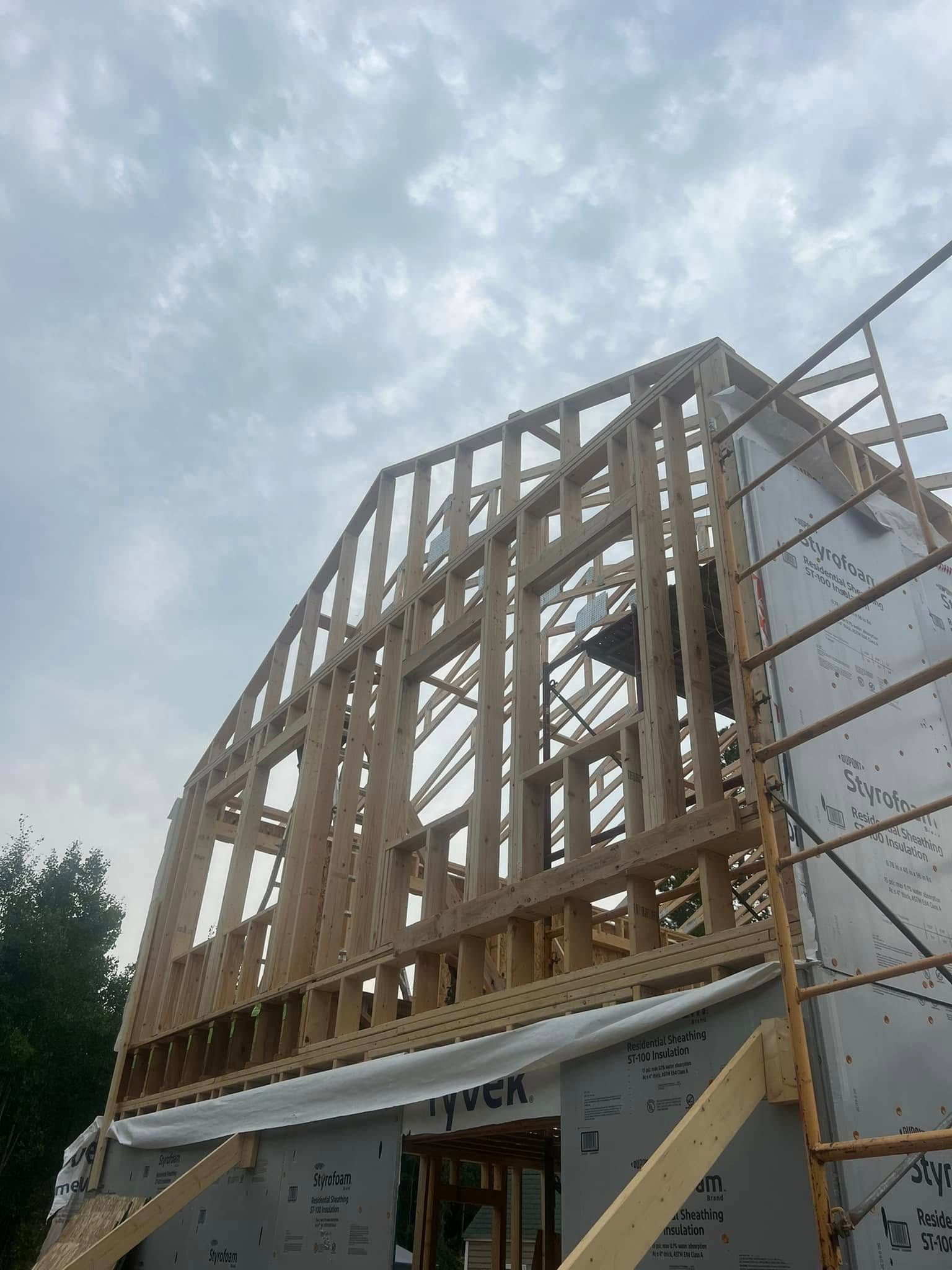 Wood-framed house under construction with scaffolding against a cloudy sky