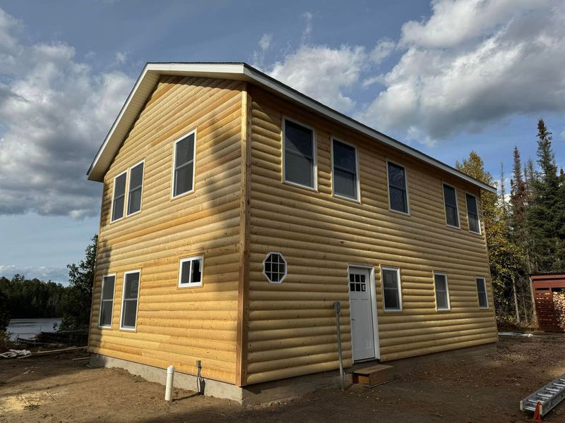 Two-story yellow log cabin with white trim and a white door under a cloudy sky