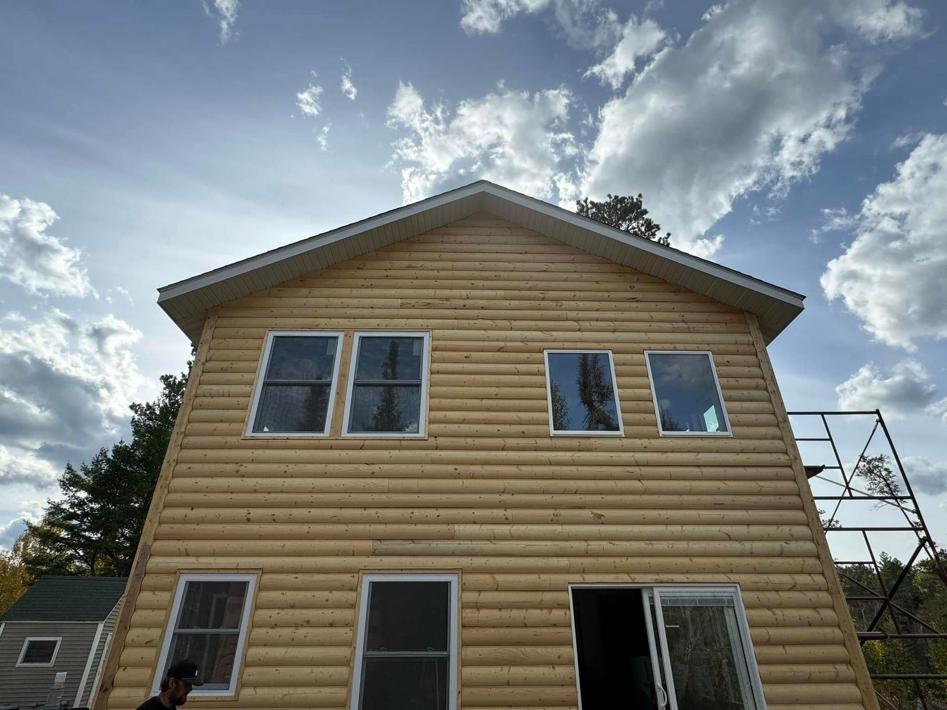 Two-story tan house under construction with unfinished siding and windows under a cloudy sky