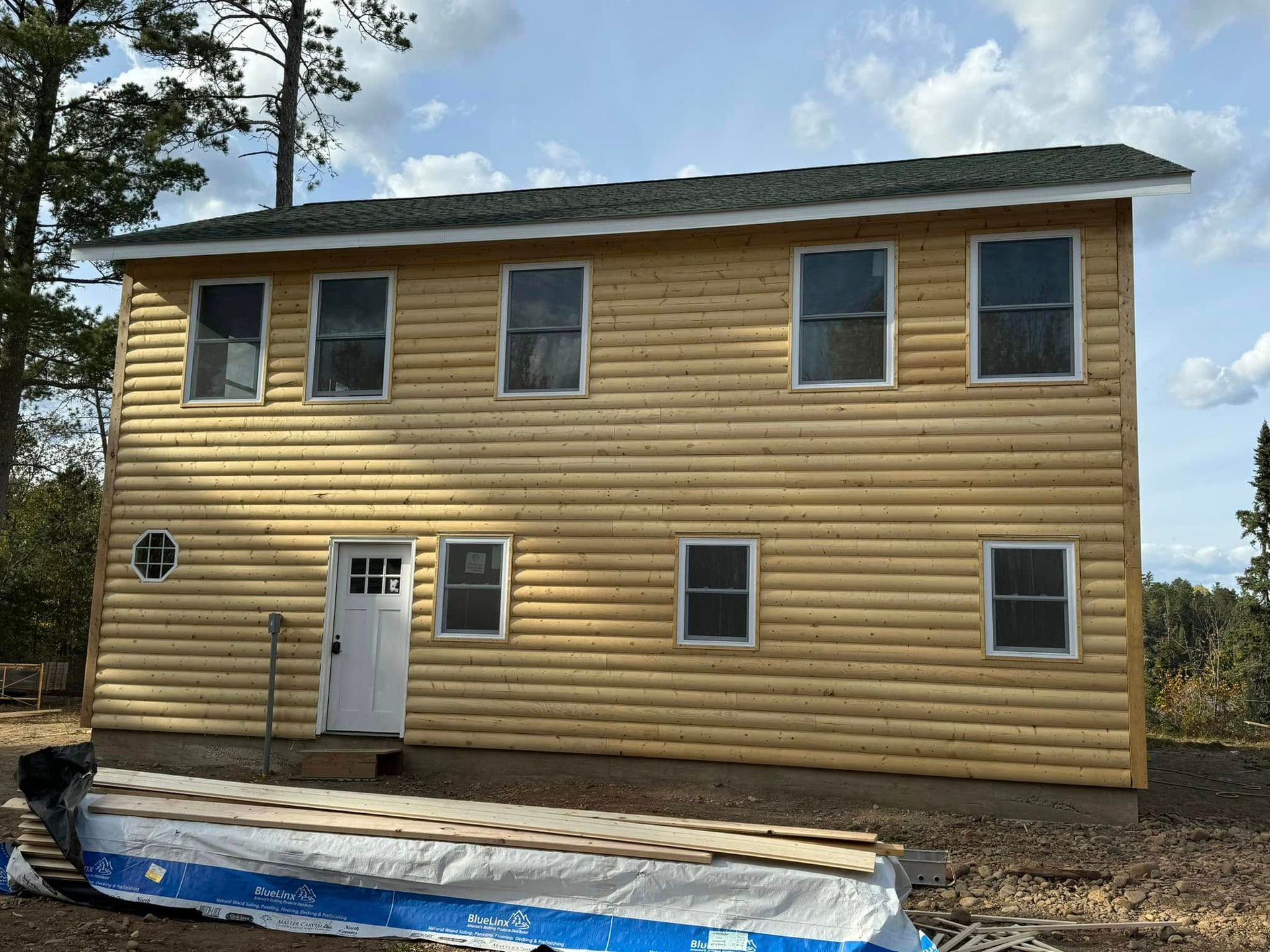 Two-story yellow house with white doors and windows under construction, with blue tarp and gravel in front