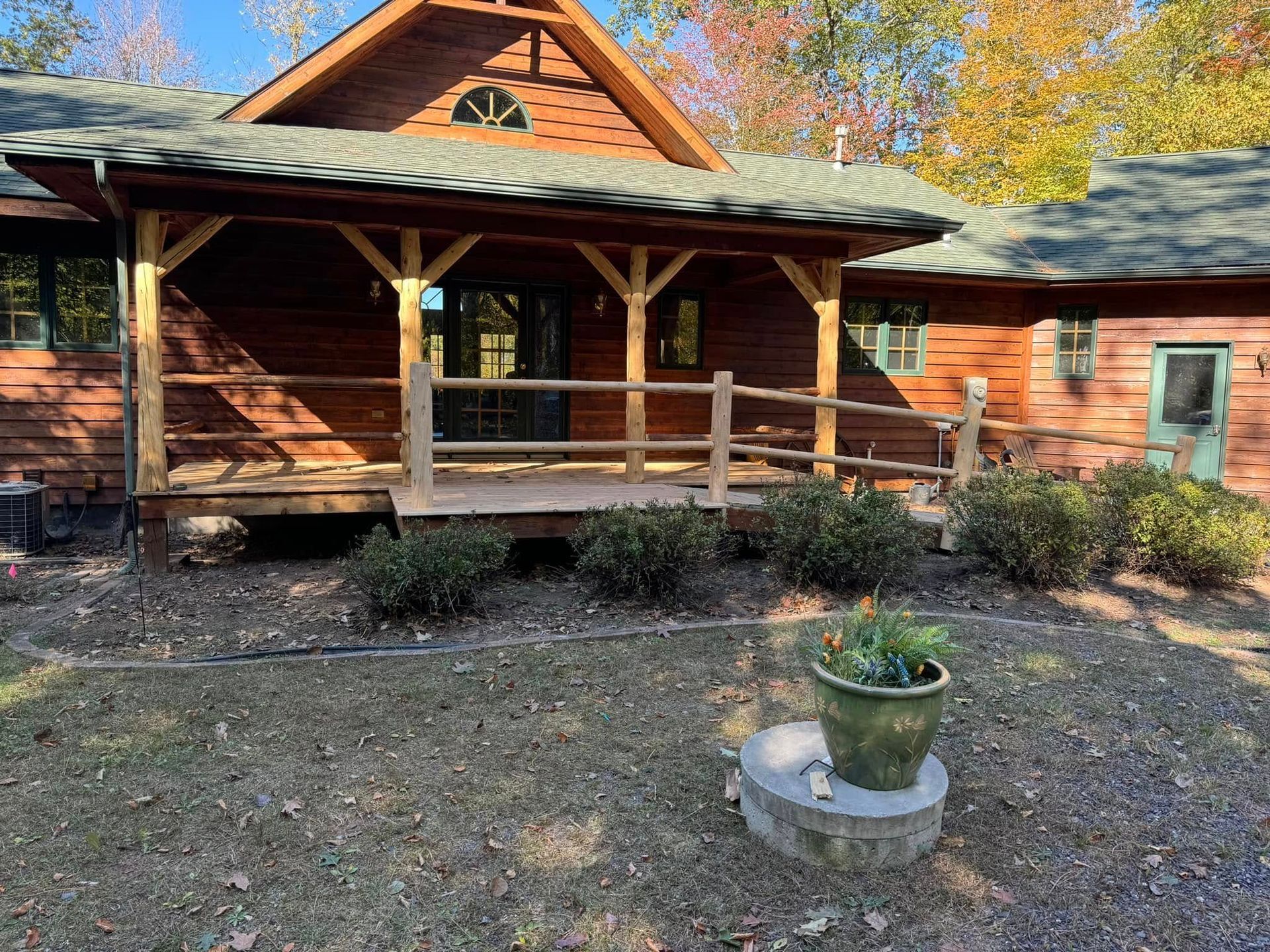 Rustic log cabin porch with railings, surrounded by autumn trees and a small planter in front