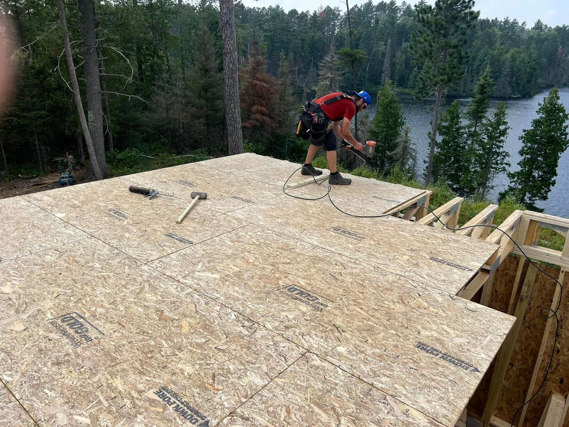 Worker installing roof sheathing on a house under construction beside a forest and lake