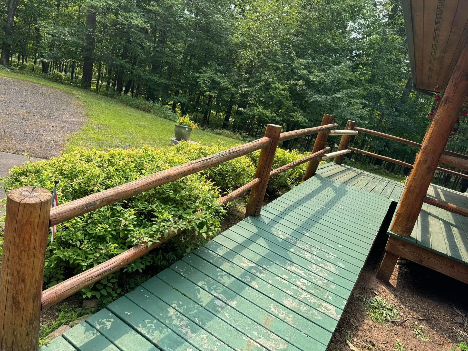 Wooden ramp with green deck boards and railings leading through a wooded yard.