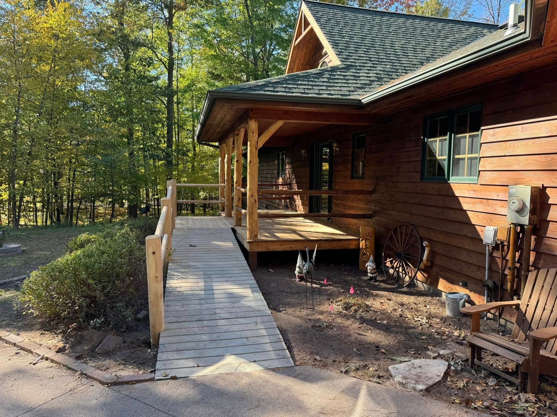 Wooden cabin porch with a ramp leading to the entrance, surrounded by trees in a forest setting.