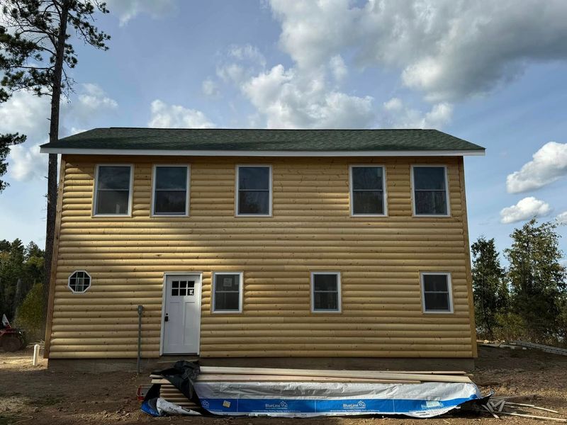 Two-story yellow house with white trim and a tarp-covered foundation under a cloudy sky