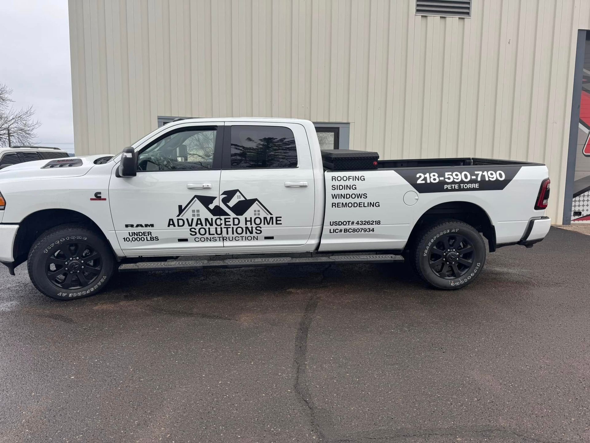 White work pickup truck with company logo and phone number parked beside a beige building.