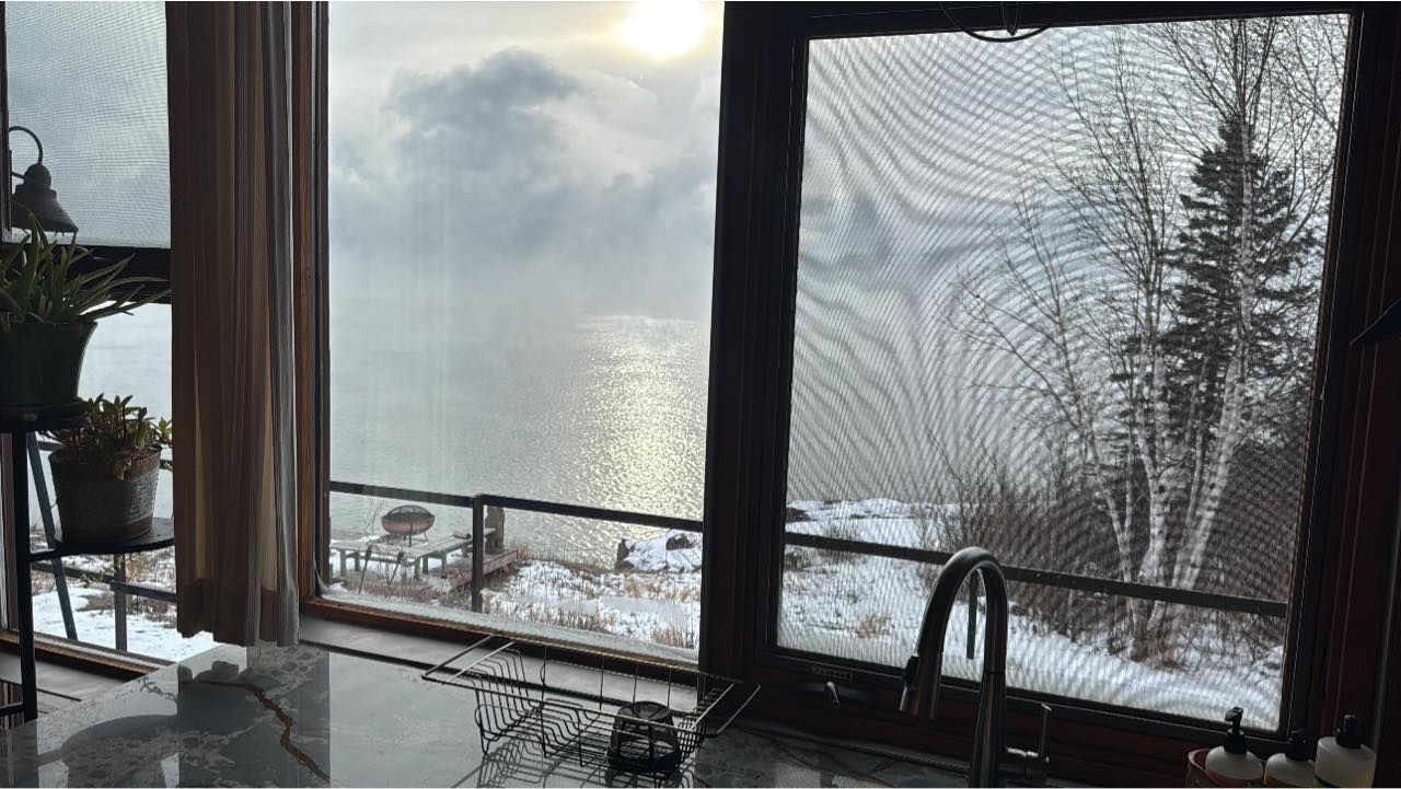 Snowy lakeside view through a cracked window over a kitchen sink