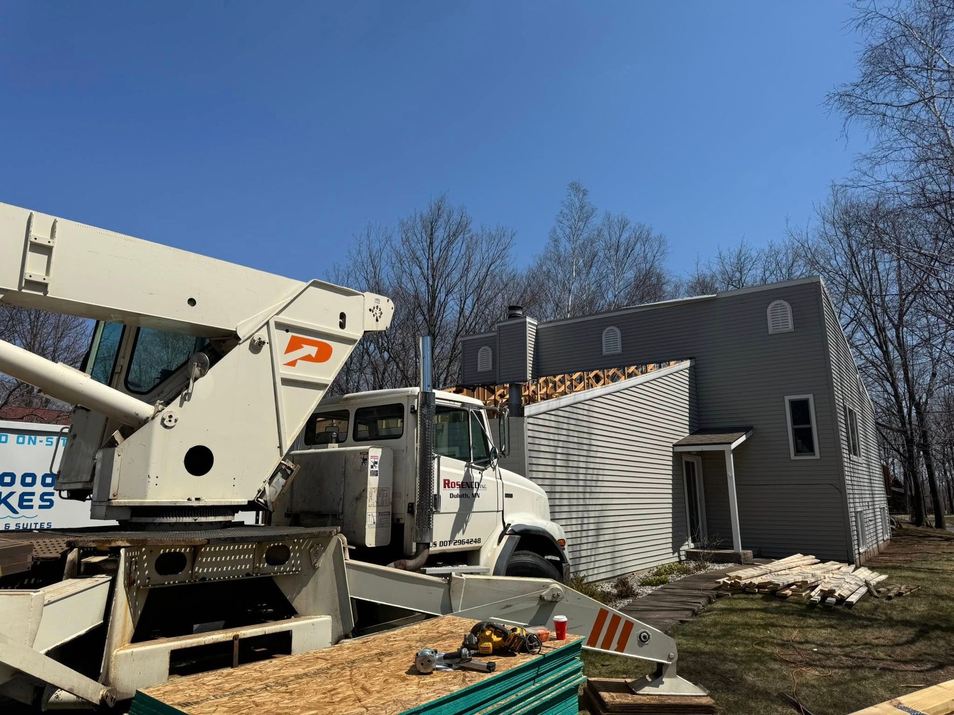 White utility truck with boom lift beside a damaged gray house under a clear blue sky