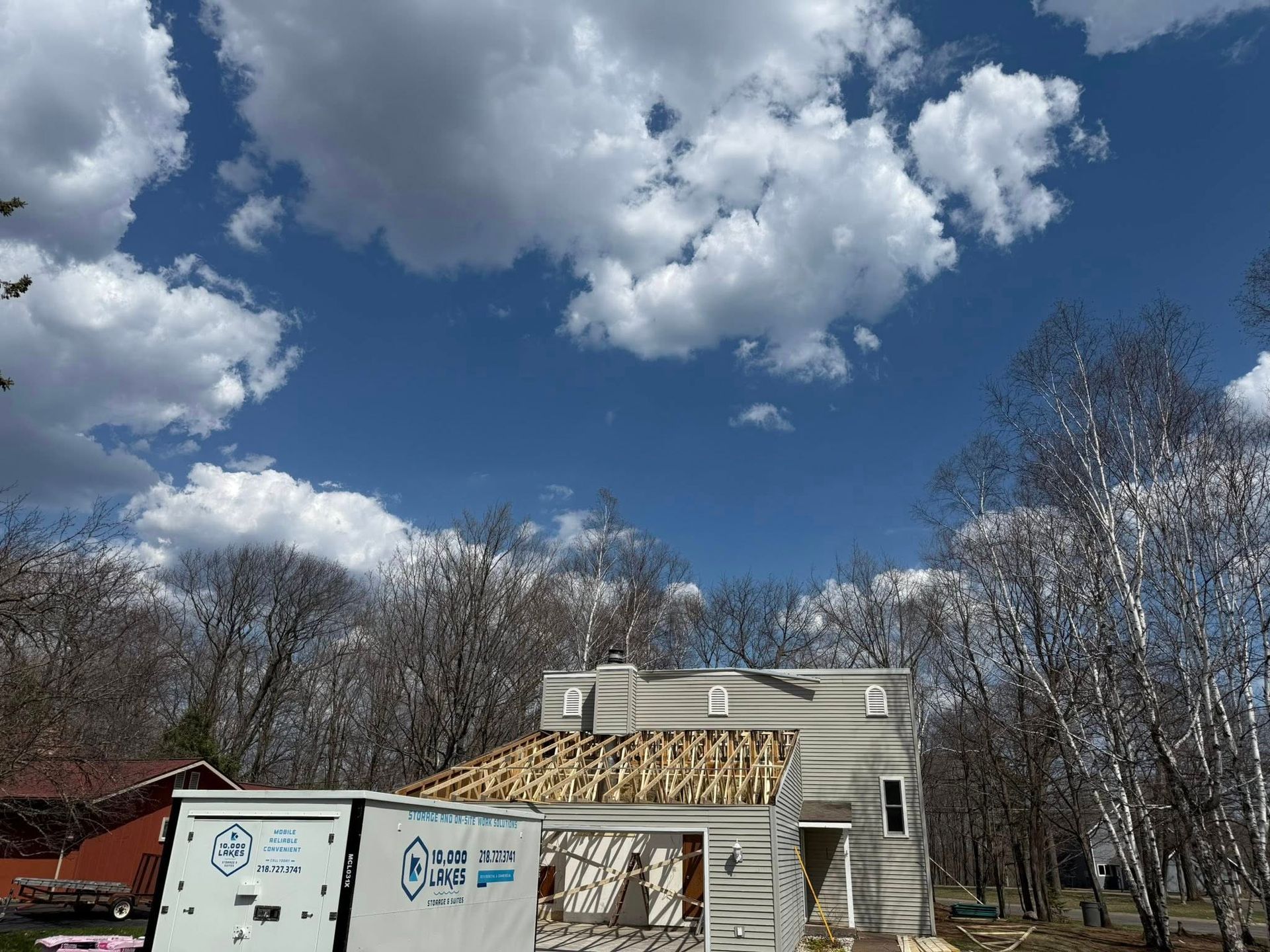 House under construction with white truck, blue sky, and clouds behind leafless trees